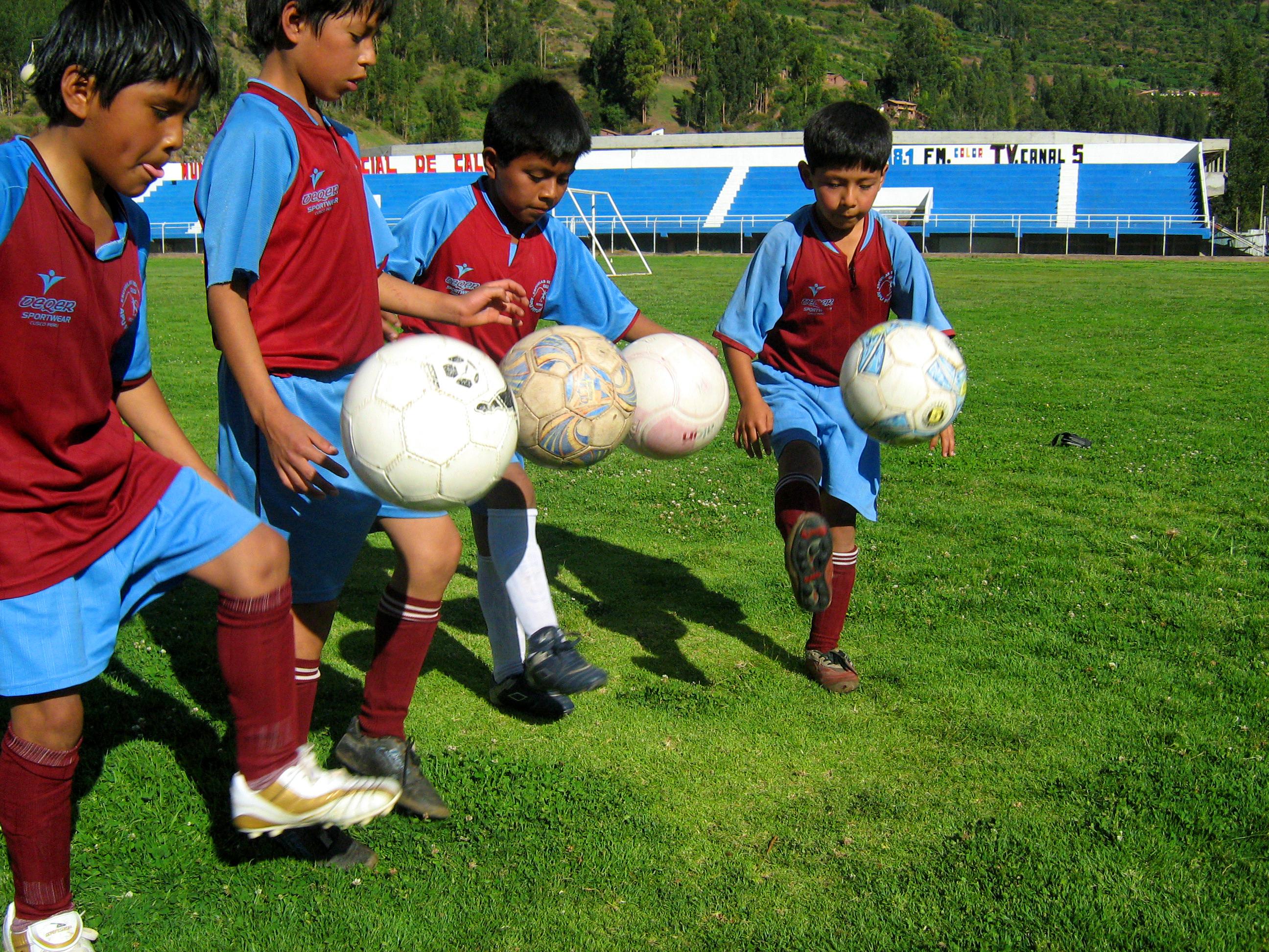 Young children practise their ball skills as part of our volunteer sports coaching project in Peru A Projects Abroad volunteer teaching sports in Peru shows children a football kicking technique